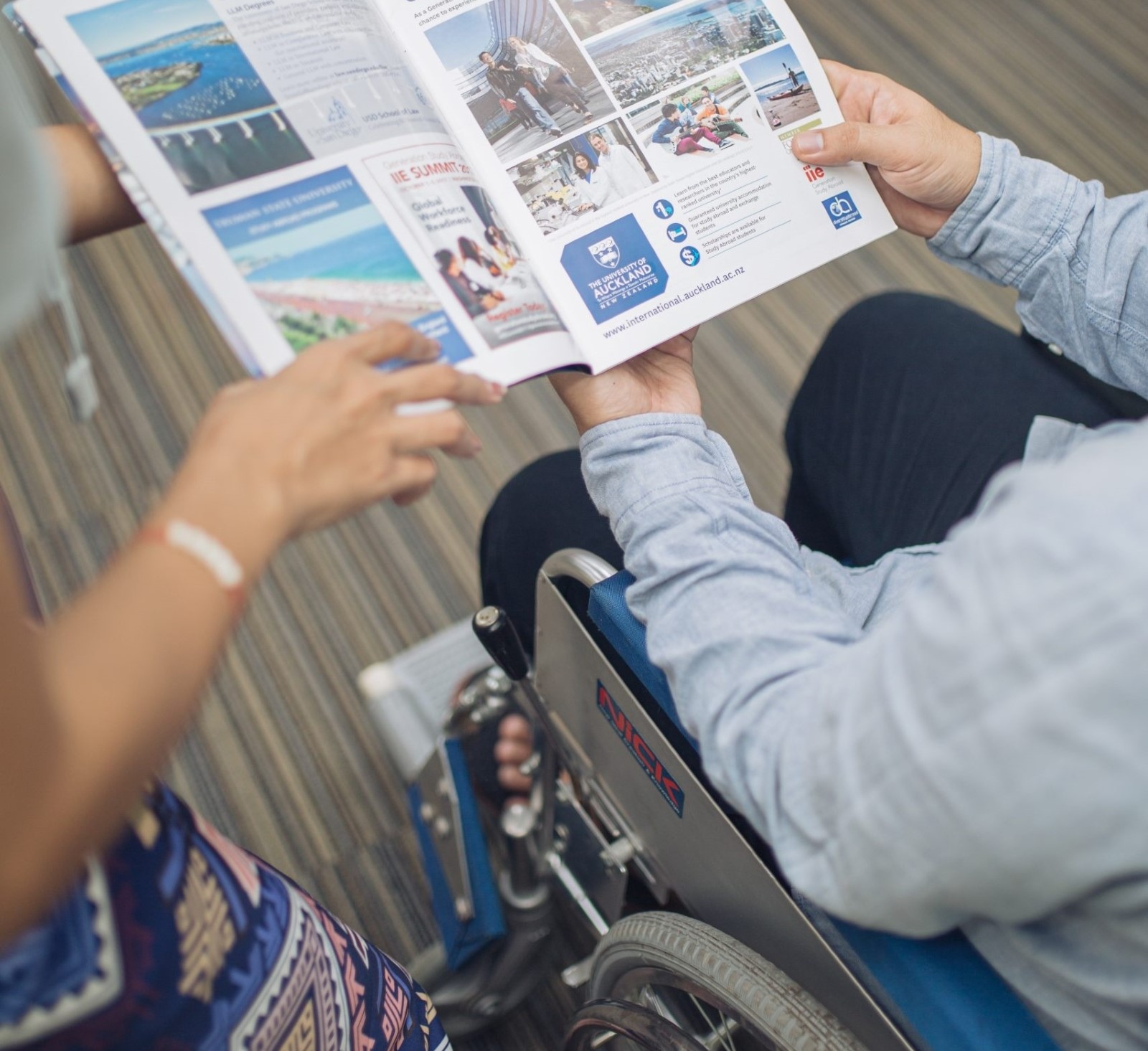 A man in a wheelchair is being guided by a female instructor as he reads.